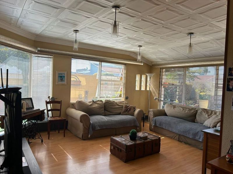 Spacious living room featuring laminate flooring, a distinctive coffered ceiling, and large windows with venetian blinds providing ample natural light.
