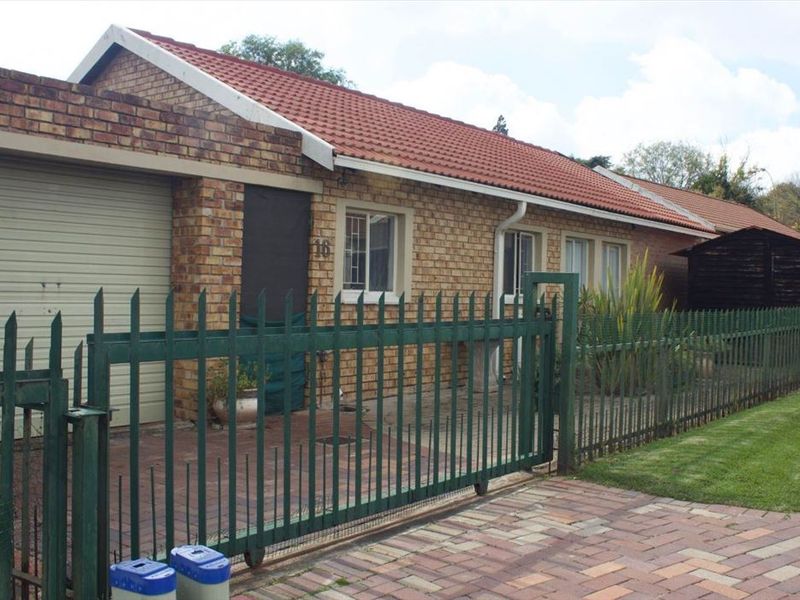 Front exterior view of a face brick townhouse featuring a tiled roof, paved driveway, and secure metal perimeter fencing.