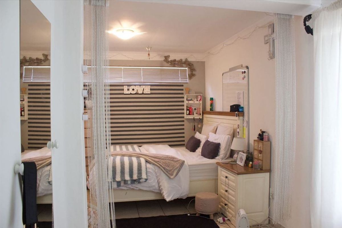 A bedroom featuring tiled flooring, a built-in mirror, and venetian blinds, offering a functional space with neutral finishes.