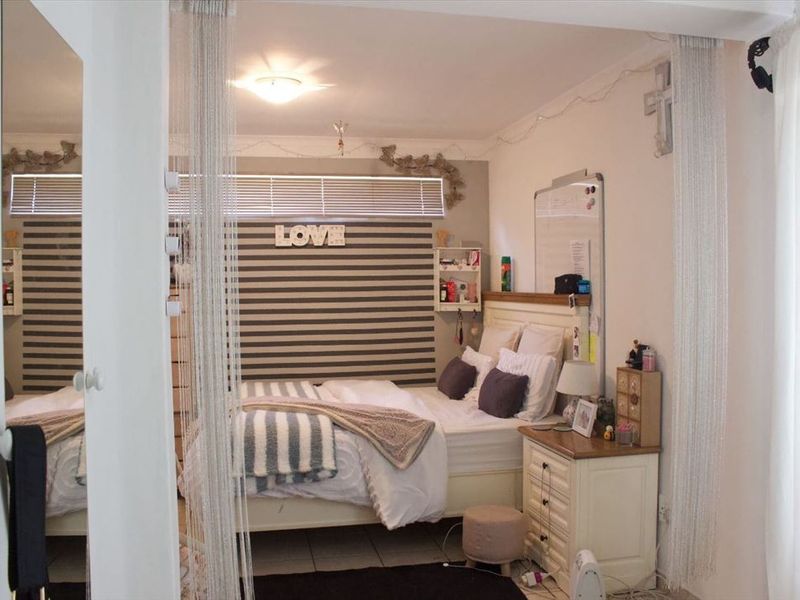 A bedroom featuring tiled flooring, a built-in mirror, and venetian blinds, offering a functional space with neutral finishes.
