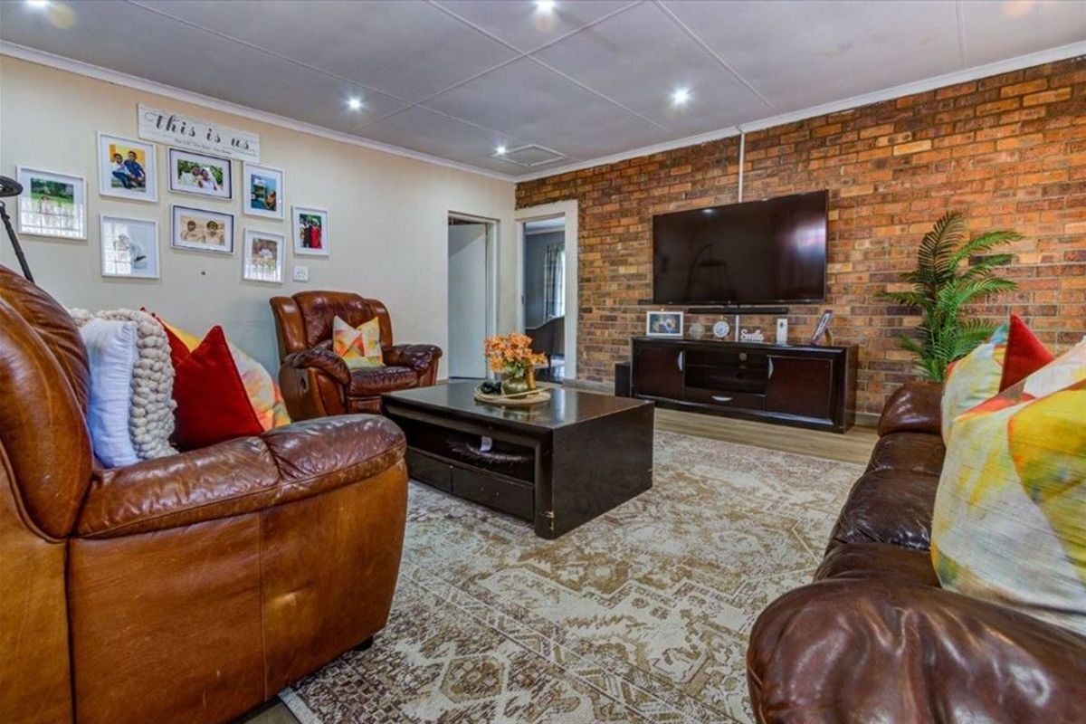 A comfortable living room featuring an exposed brick feature wall, recessed downlighting, and tiled ceiling panels, creating a warm and inviting atmosphere.