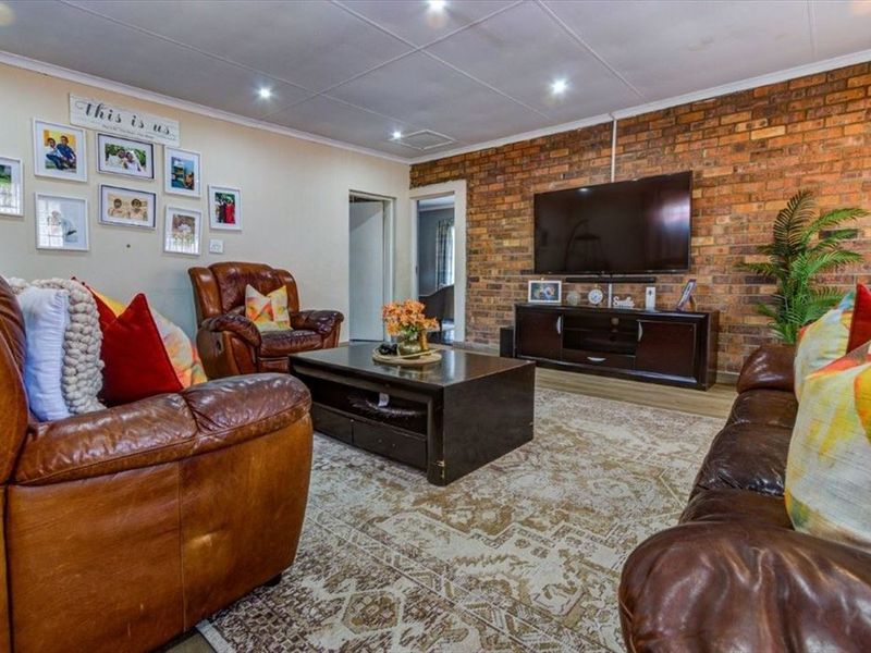 A comfortable living room featuring an exposed brick feature wall, recessed downlighting, and tiled ceiling panels, creating a warm and inviting atmosphere.