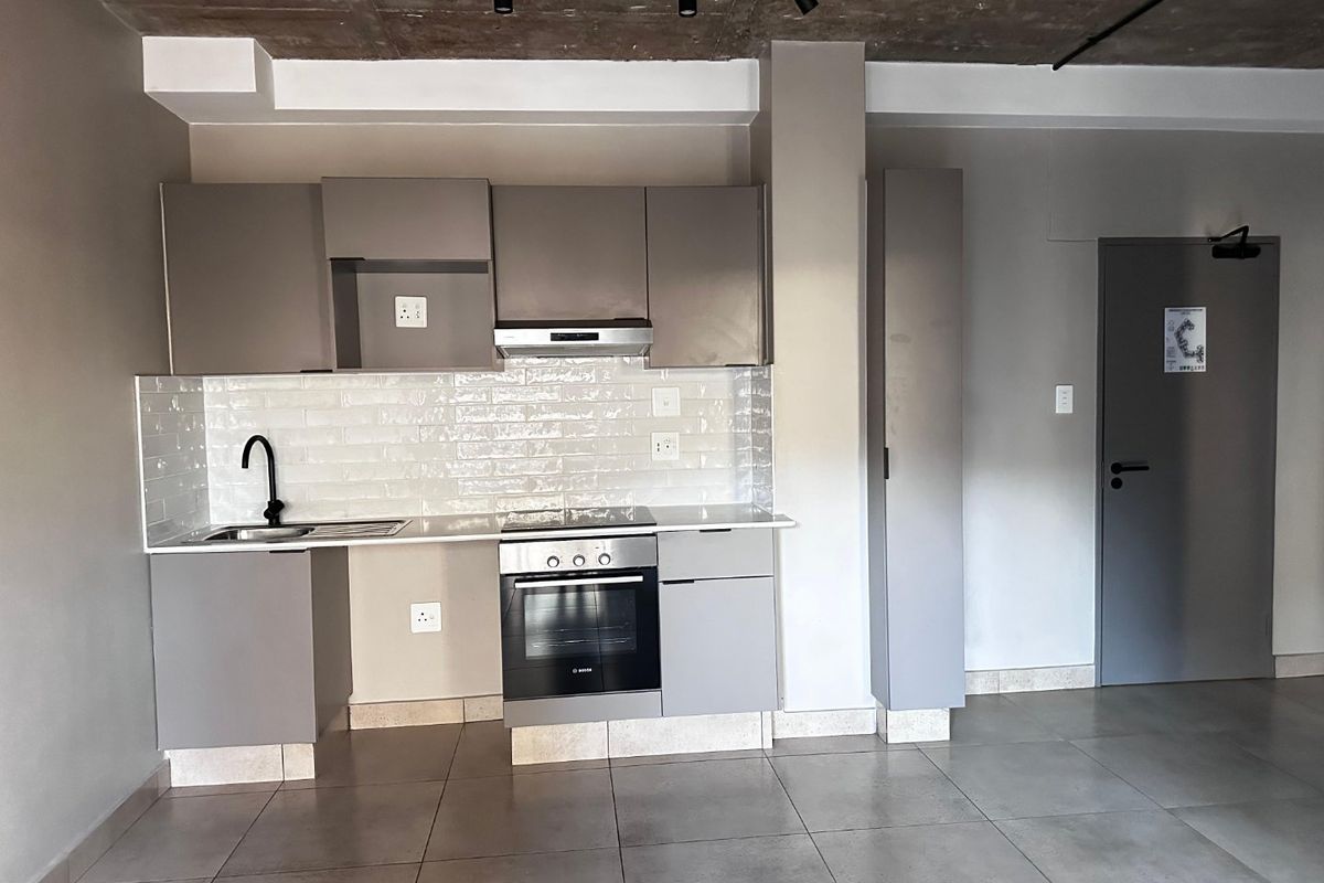 Modern kitchen featuring sleek grey cabinetry, subway tile backsplash, built-in oven and hob, and an industrial-style exposed concrete ceiling.
