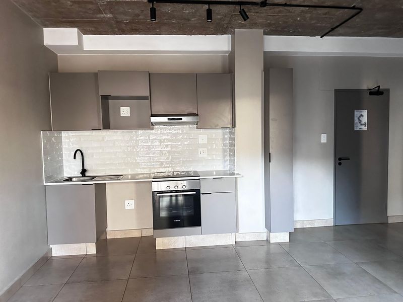 Modern kitchen featuring sleek grey cabinetry, subway tile backsplash, built-in oven and hob, and an industrial-style exposed concrete ceiling.