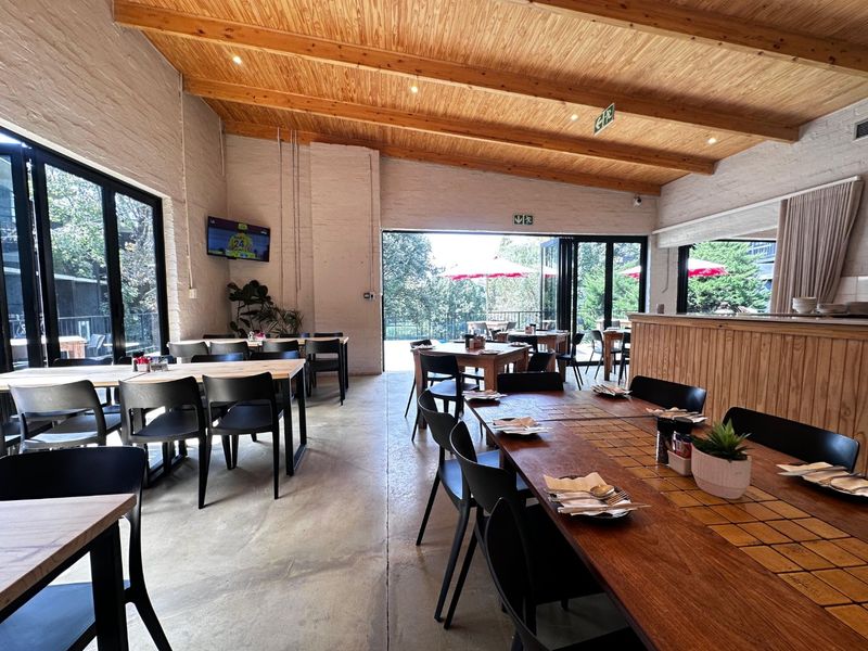 Spacious open-plan dining area featuring exposed timber beam ceilings, polished concrete floors, and large bi-fold doors opening to an outdoor patio.