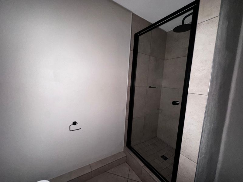 A modern bathroom featuring a walk-in shower with a sleek black frame, rainfall shower head, and neutral wall and floor tiling.