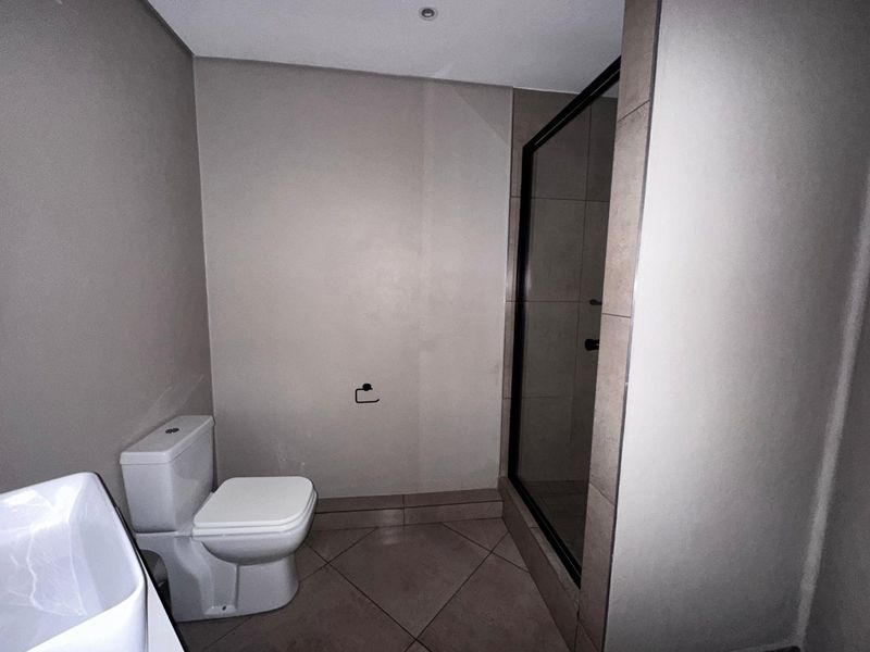 A clean, modern bathroom featuring a tiled shower enclosure, a standard toilet, and neutral wall finishes.