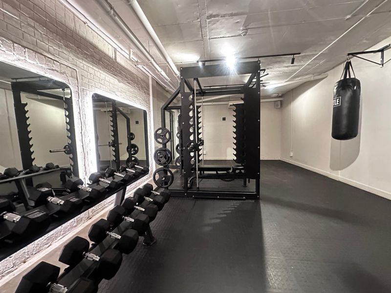 A well-equipped private gym featuring rubber flooring, exposed industrial-style ceiling, brick accent wall, and large wall-mounted mirrors.