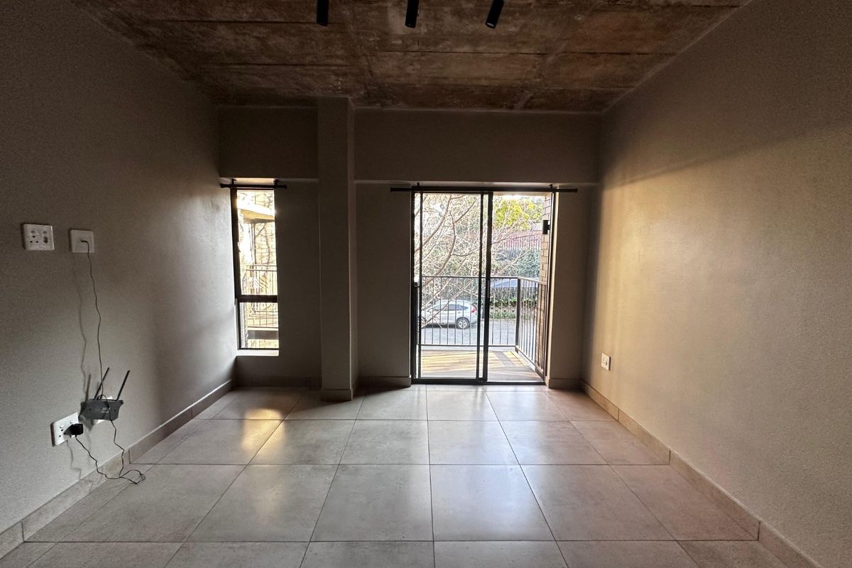 An open-plan living area featuring an industrial-style exposed concrete ceiling, tiled flooring, and a sliding glass door leading to a private balcony.