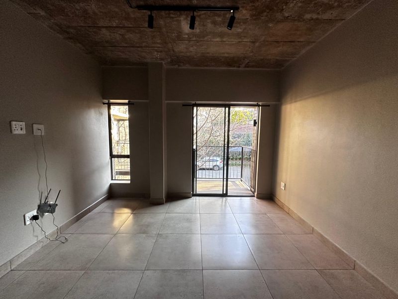 An open-plan living area featuring an industrial-style exposed concrete ceiling, tiled flooring, and a sliding glass door leading to a private balcony.
