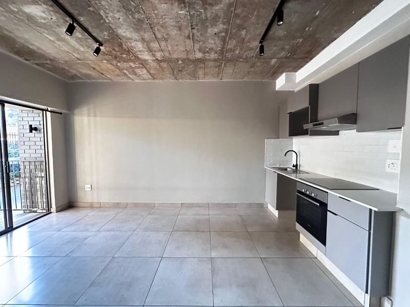 Modern open-plan living area featuring an exposed concrete ceiling, sleek grey cabinetry, integrated kitchen appliances, and direct access to a private balcony.