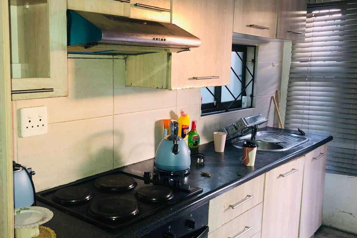 A compact kitchen featuring light wood-finish cabinetry, a built-in oven and hob, stainless steel sink, and tiled flooring, requiring some cosmetic updates.