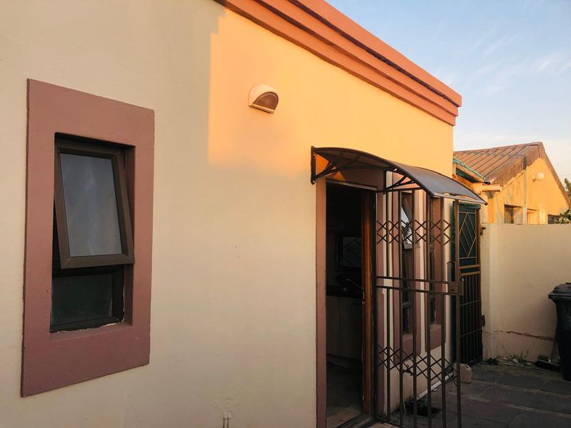 Rear exterior view of the property featuring a security gate, protective awning over the entrance, and paved patio area.