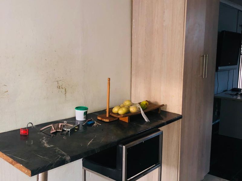 A small kitchen area featuring a stone breakfast bar, built-in cabinetry, and tiled flooring, currently showing signs of wear and wall staining.