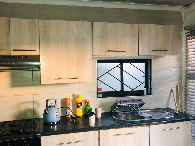 Compact kitchen featuring light wood-look cabinetry, dark countertops, built-in oven and hob, and tiled backsplash, requiring ceiling and finish repairs.