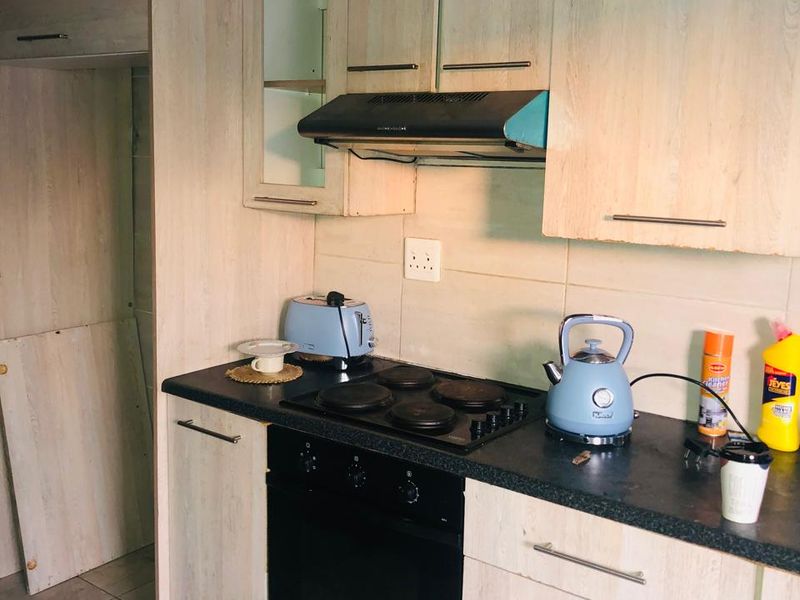 A dated kitchen featuring light wood-look cabinetry, dark laminate countertops, and built-in cooking appliances, requiring maintenance and cosmetic updates.