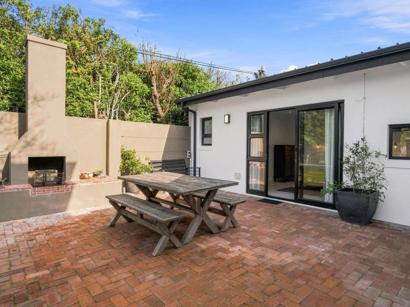 A well-maintained outdoor patio featuring brick paving, a built-in fireplace, and direct access to the interior through sliding glass doors.