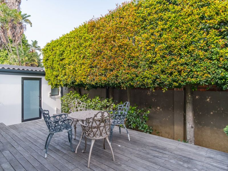 A private outdoor patio area featuring timber decking, enclosed by a high boundary wall and mature privacy hedging.