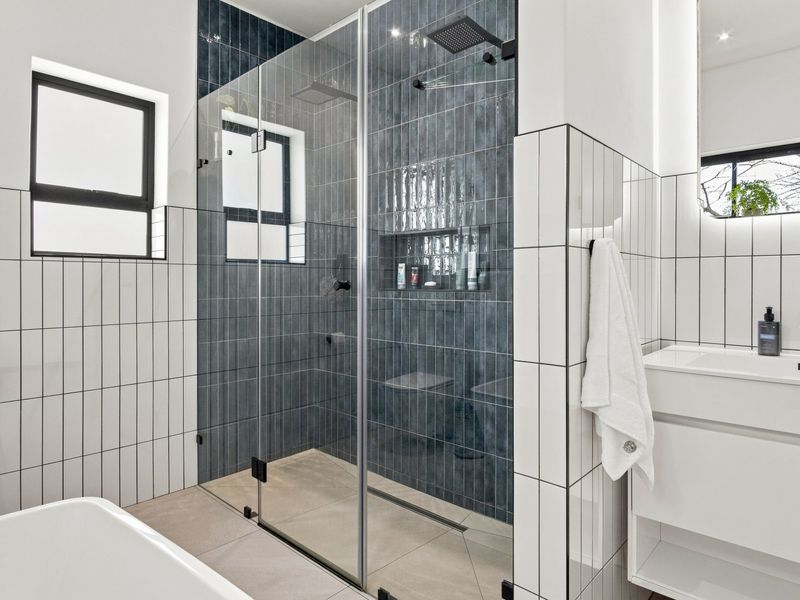 Modern bathroom featuring a walk-in shower with blue feature tiling, a built-in niche, black fixtures, a vanity unit, and a freestanding bathtub.