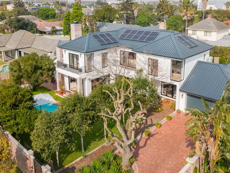 Aerial view of a modern two-story house featuring a metal roof with solar panels, a swimming pool, and a paved driveway.