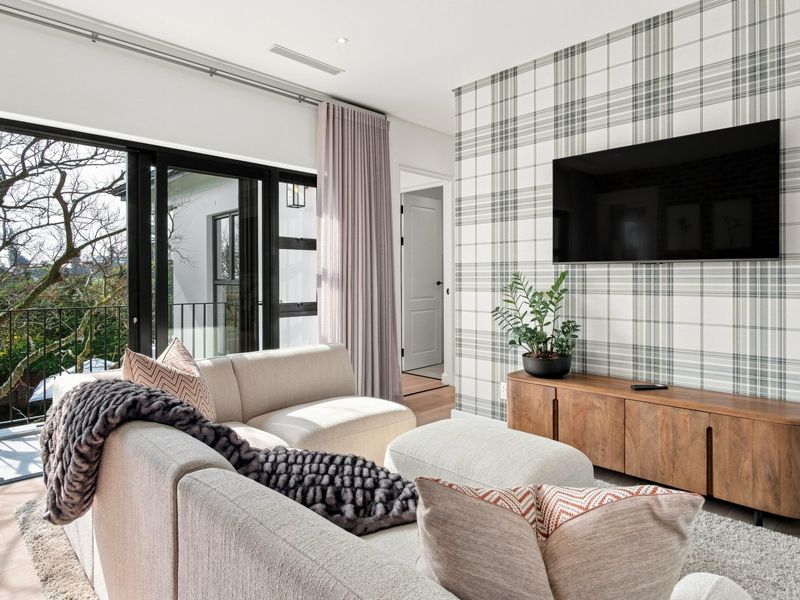 A modern living room featuring a feature wallpaper wall, large sliding glass doors leading to a balcony, and integrated ceiling lighting.
