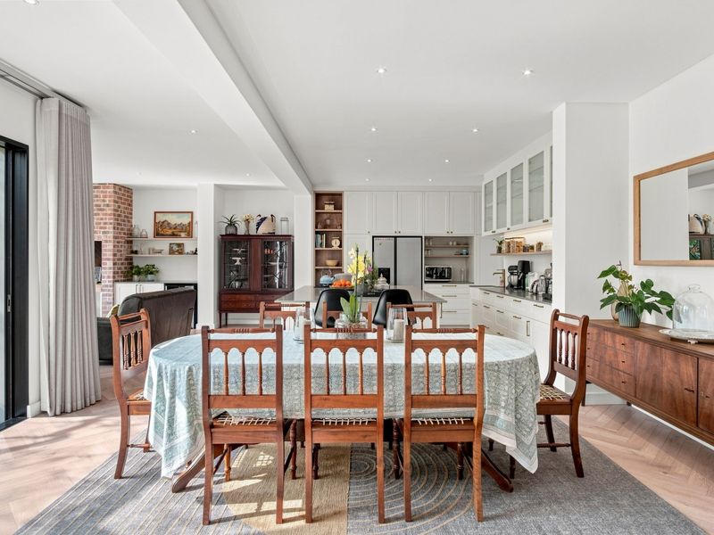 Spacious open-plan living and dining area featuring herringbone timber flooring, modern kitchen cabinetry, and seamless access to the outdoor patio through sliding glass doors.