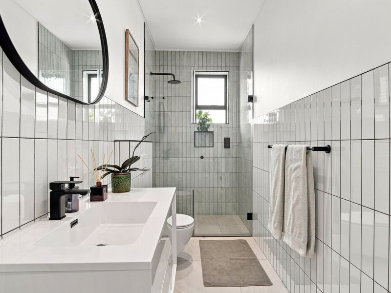 Modern bathroom featuring a sleek vanity, walk-in shower with glass screen, wall-mounted toilet, and contemporary tiled finishes with matte black fixtures.