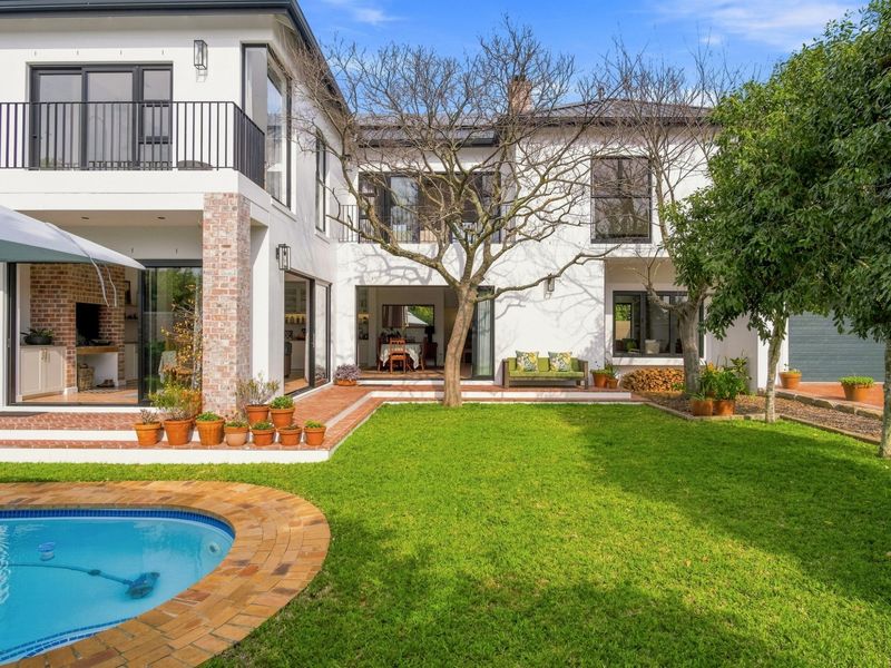 A well-maintained rear exterior featuring a swimming pool, brick-paved patio area, landscaped garden, and a two-story home with balcony access.