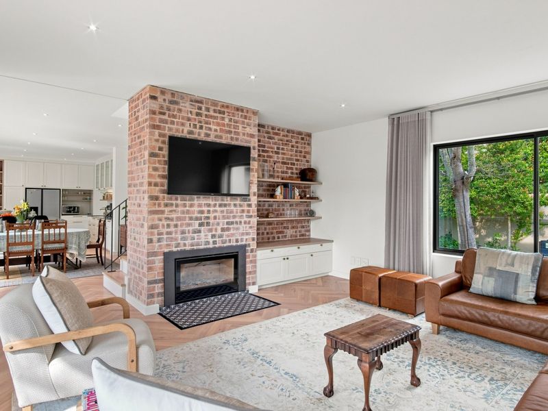 Spacious open-plan living area featuring a striking exposed brick fireplace, herringbone timber flooring, and seamless flow to the adjacent kitchen and dining space.