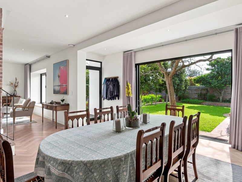 Spacious open-plan dining and living area featuring herringbone timber flooring, exposed brick accents, and large sliding doors opening to a lush garden.