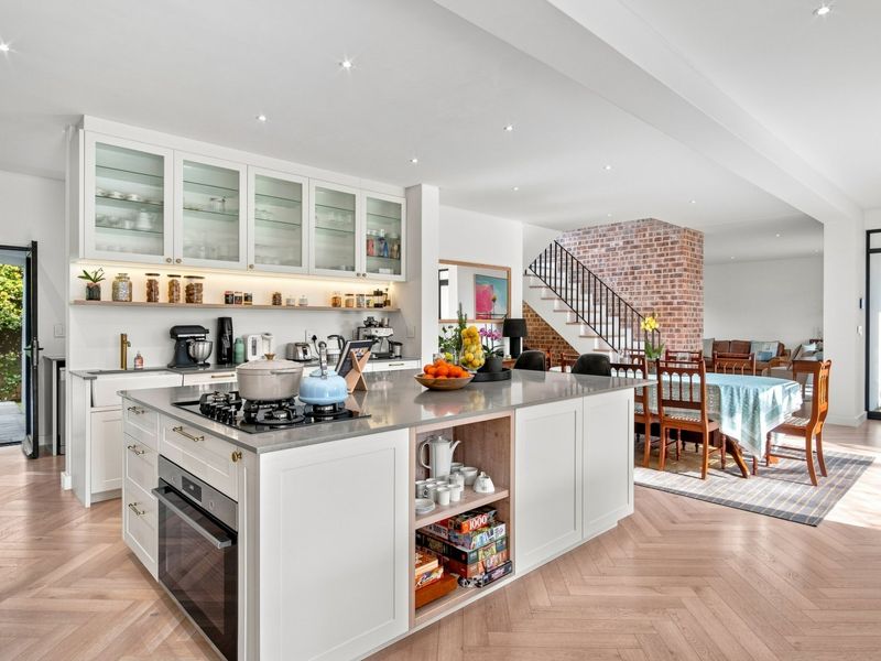 Spacious open-plan kitchen and dining area featuring a large central island, herringbone timber flooring, and an exposed brick feature wall with a staircase.