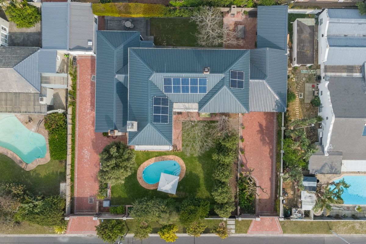 Aerial view of the property featuring a metal roof with solar panels, a swimming pool, paved driveway, and established garden areas.