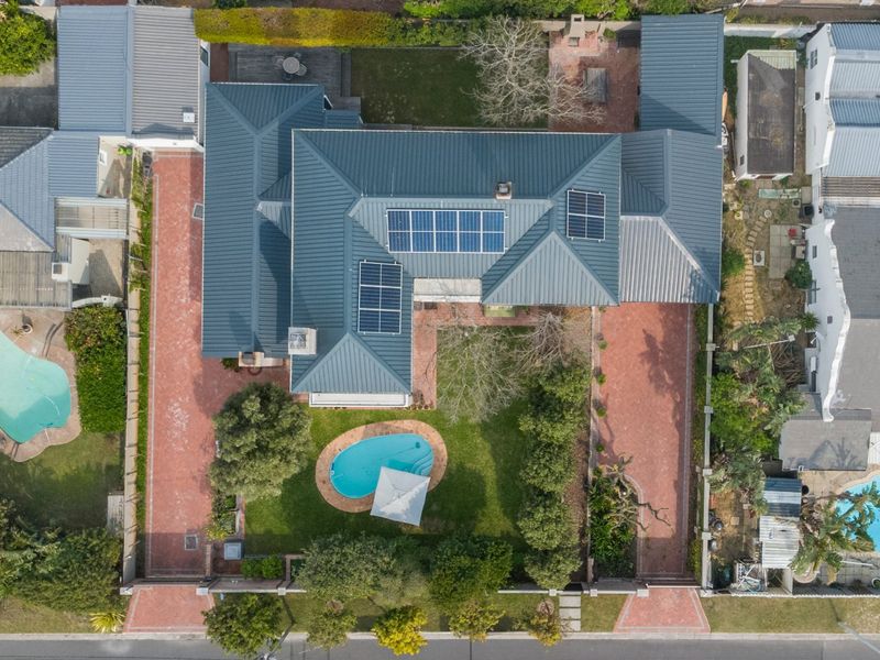 Aerial view of the property featuring a metal roof with solar panels, a swimming pool, paved driveway, and established garden areas.