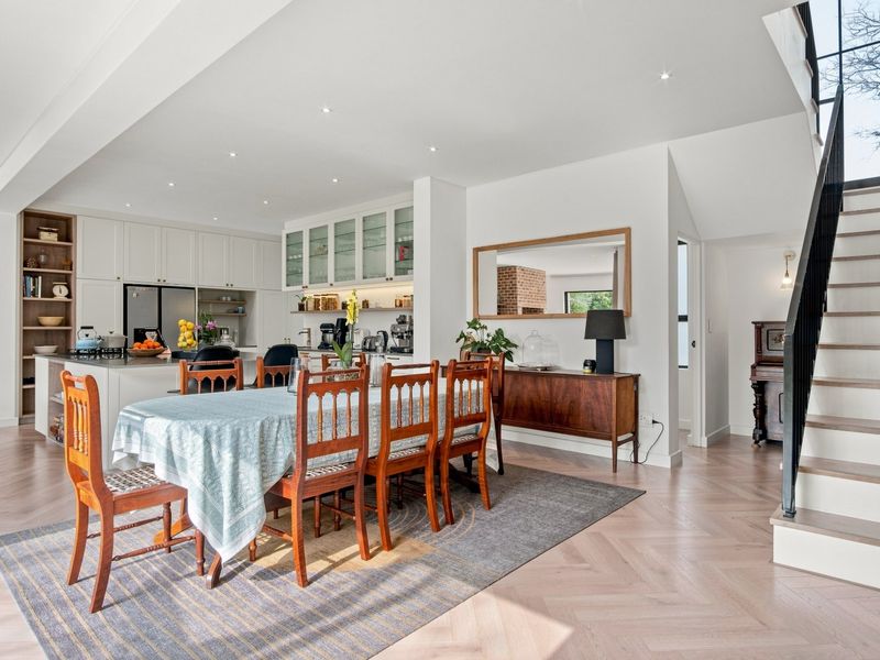 Spacious open-plan living area featuring herringbone timber flooring, a modern kitchen with island, and a staircase with a sleek metal balustrade.
