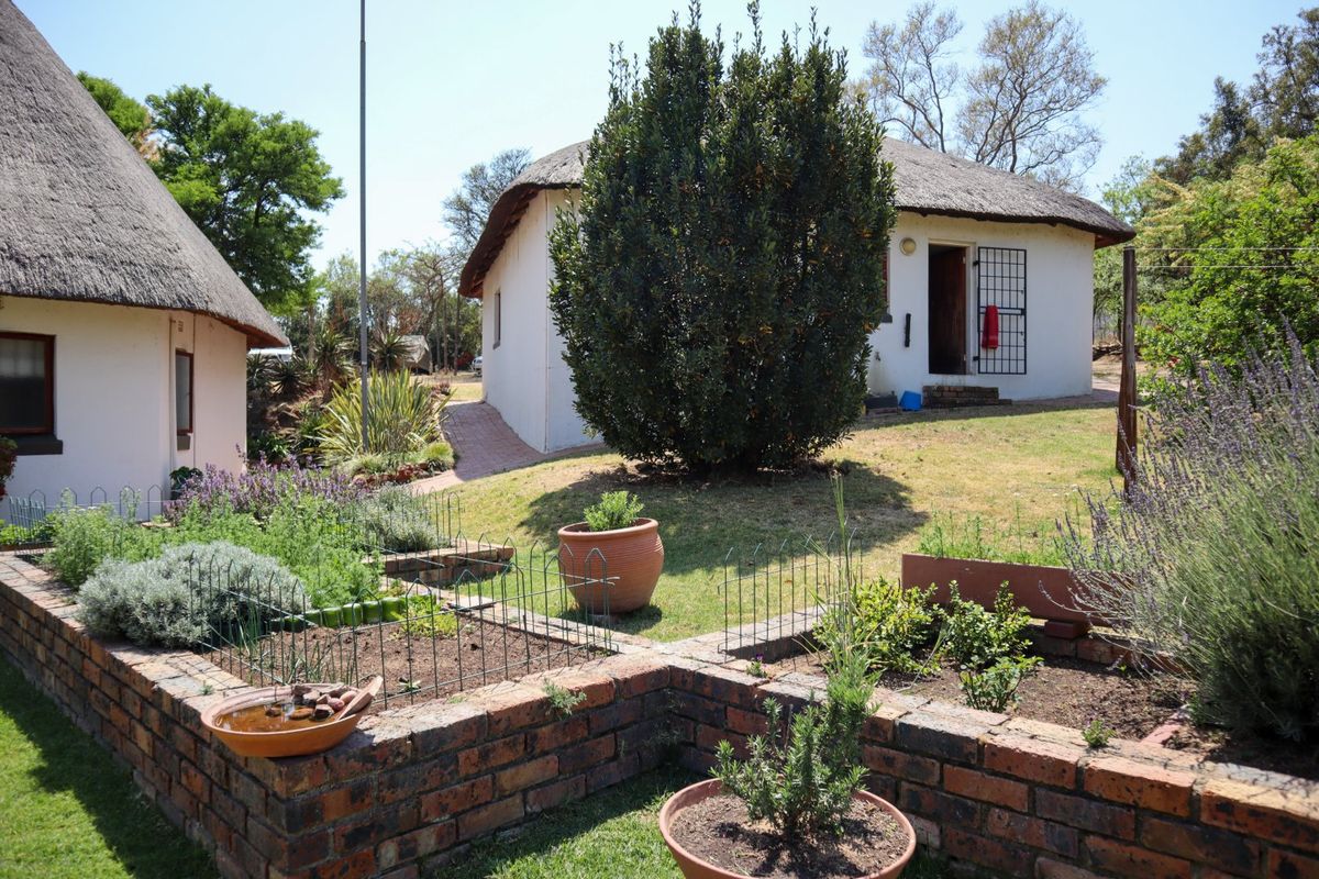 A view of the rear garden featuring a well-maintained lawn, brick-edged garden beds, and traditional thatch-roofed farm buildings.
