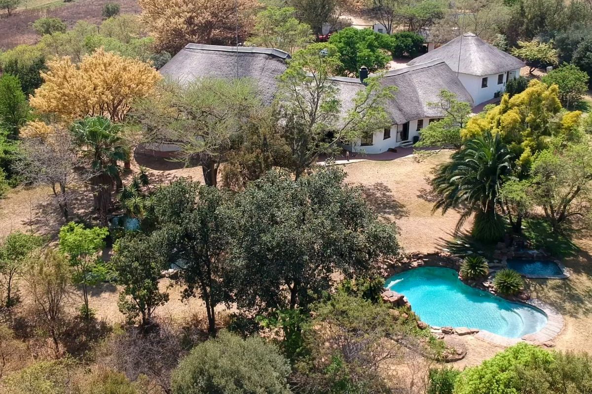 Aerial view of a farm property featuring a large thatched-roof residence, mature garden, and a natural-style rock swimming pool.