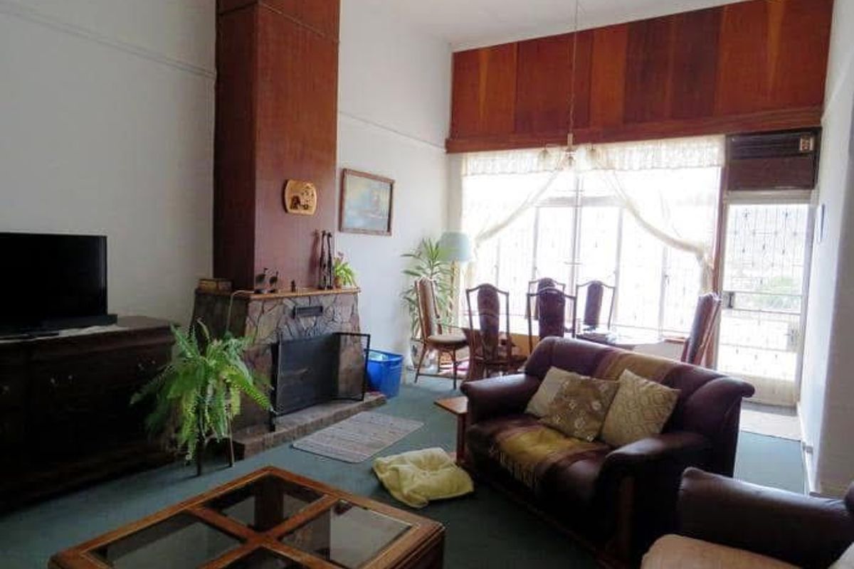 Spacious living room featuring a prominent stone fireplace, high ceilings with wood paneling, and large windows providing natural light.