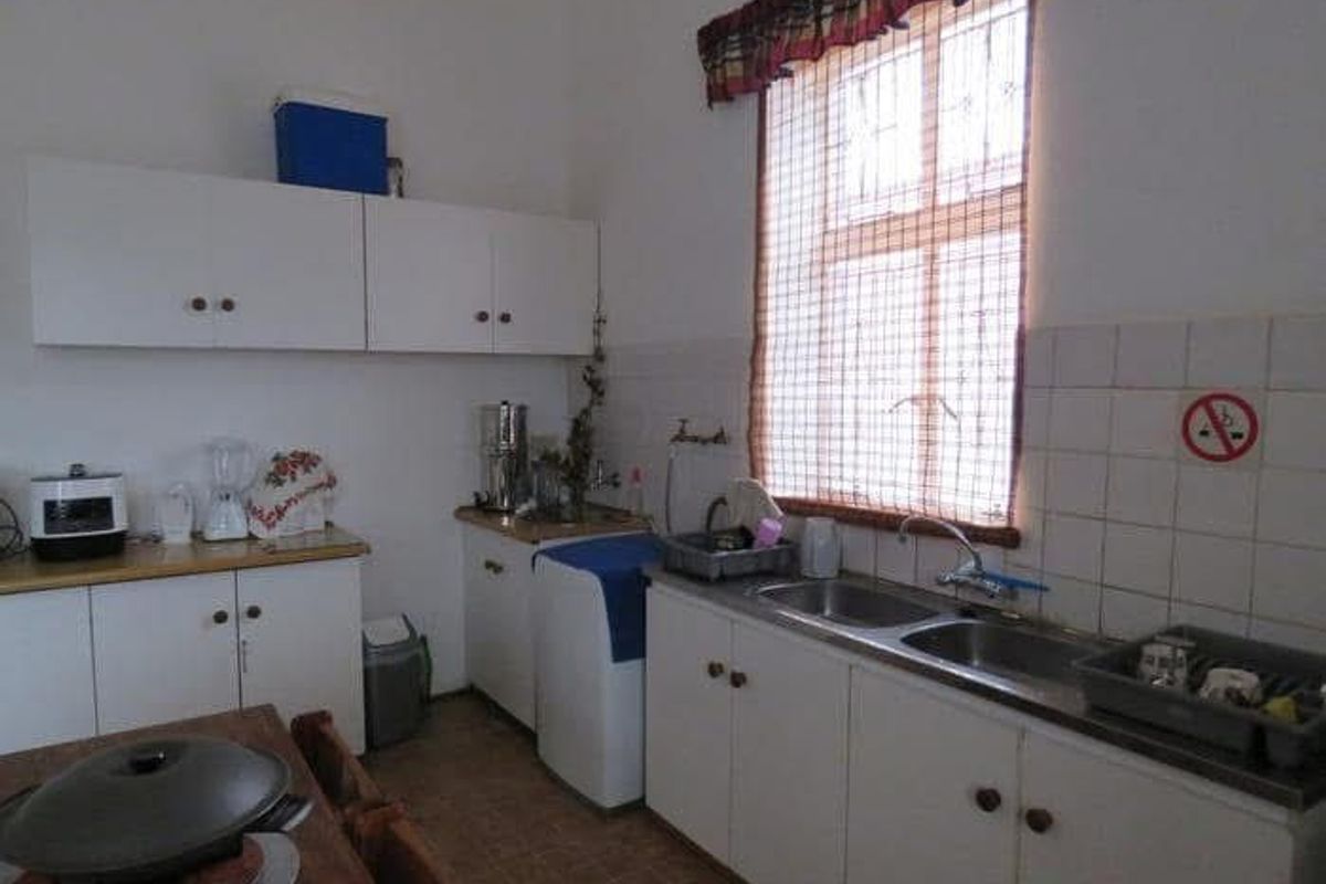 A functional kitchen featuring white built-in cabinetry, a double basin sink, and tiled splashbacks, offering a dated but practical layout.