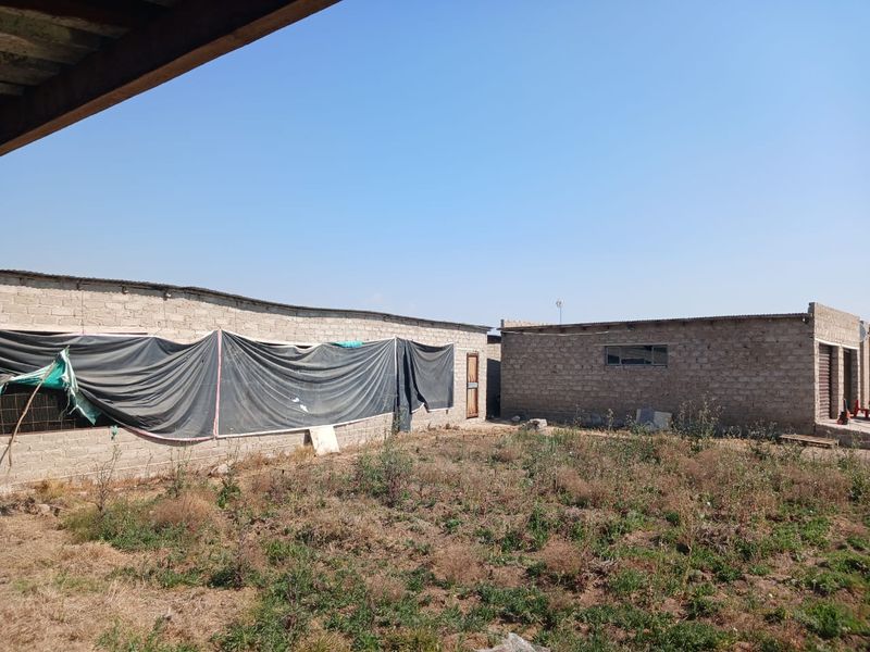 Rear view of farm outbuildings featuring exposed brick construction and corrugated metal roofing, set within an undeveloped yard area.