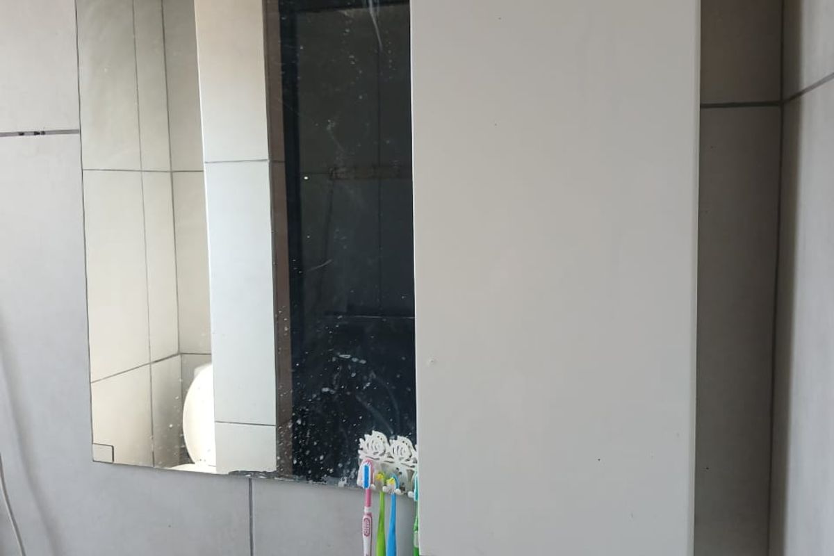 A bathroom vanity area featuring a wall-mounted basin, chrome mixer tap, and a wall-mounted medicine cabinet with a damaged mirror.