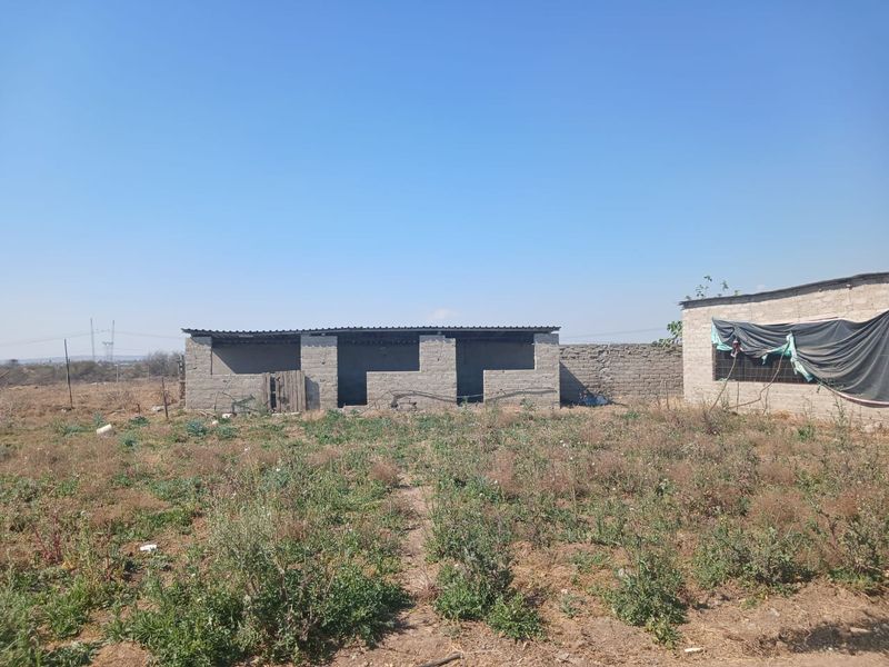 An exterior view of an unfinished concrete block structure on a rural farm property, featuring a corrugated metal roof and surrounding land.