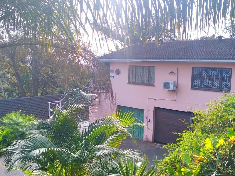 Front elevation of a two-story residential property featuring a tiled roof, garage access, and security-fitted windows, surrounded by established garden foliage.