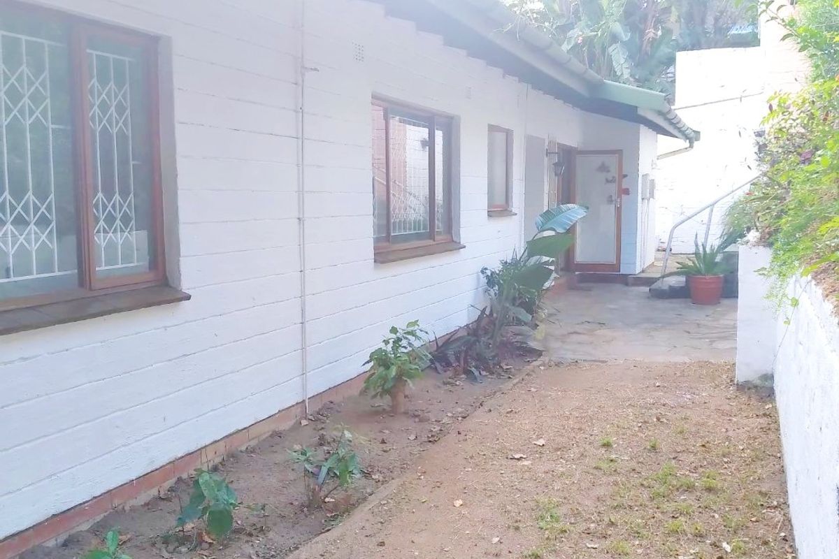 A view of the rear exterior of the property featuring a concrete pathway, painted brick walls, and security-fitted windows.