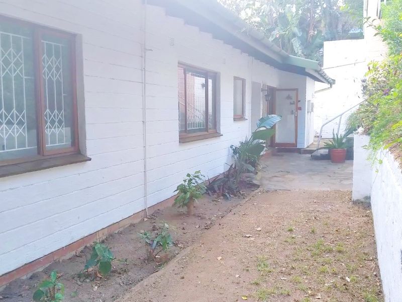 A view of the rear exterior of the property featuring a concrete pathway, painted brick walls, and security-fitted windows.