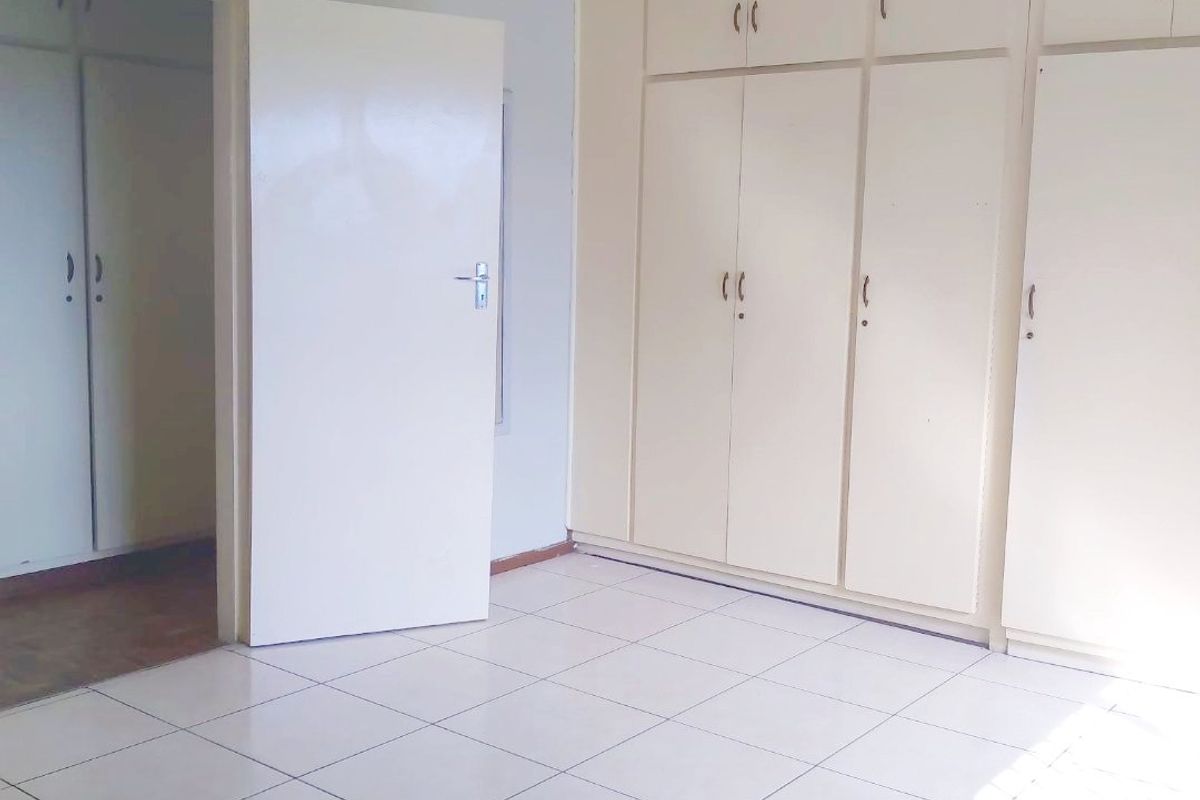 A vacant bedroom featuring tiled flooring and extensive built-in cupboard storage with a neutral color palette.