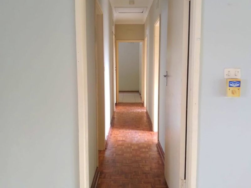 A long, empty hallway featuring traditional parquet flooring, multiple doorways, and a ceiling access hatch, providing access to various rooms in the home.