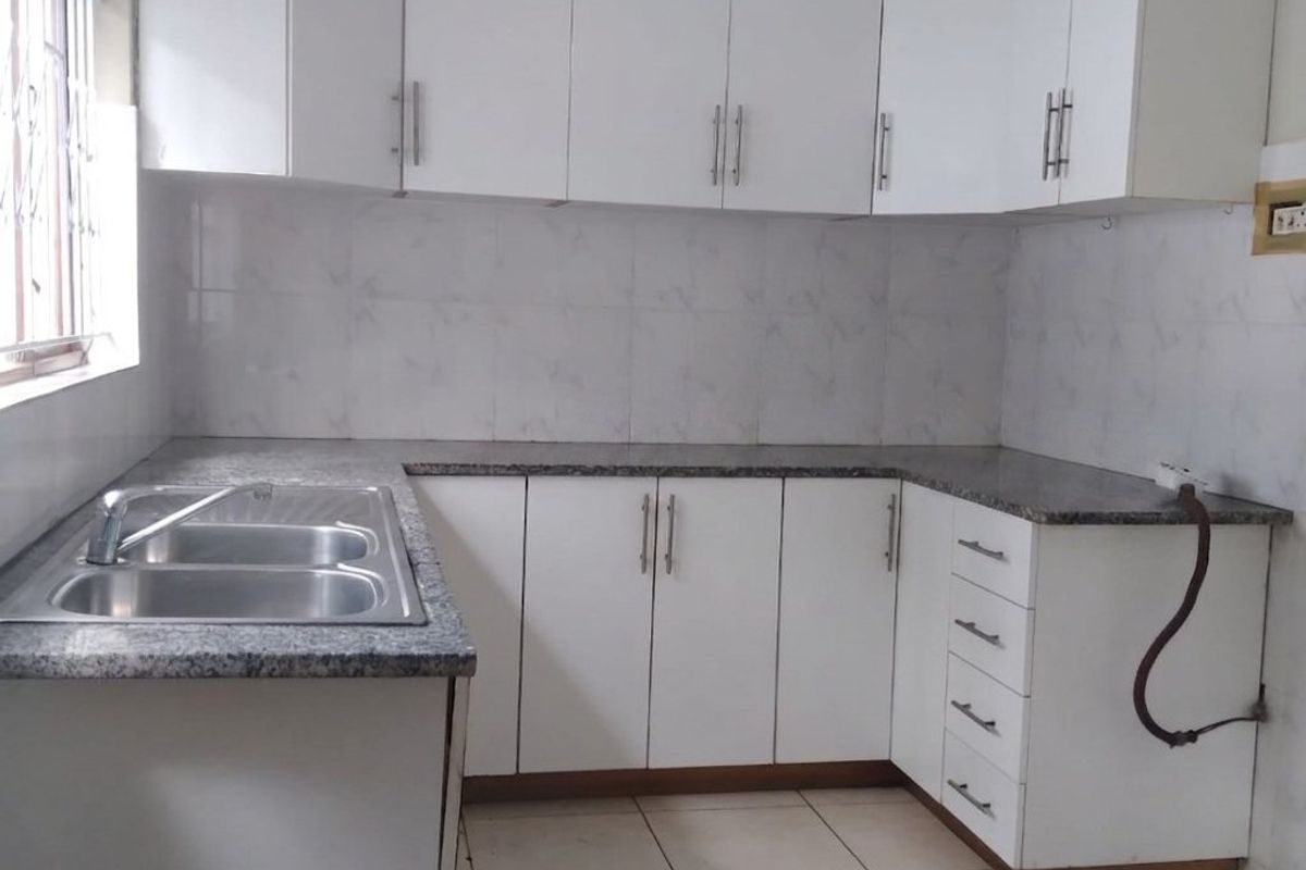 A clean, functional kitchen featuring white cabinetry, granite countertops, a double stainless steel sink, and tiled flooring, ready for personalization.