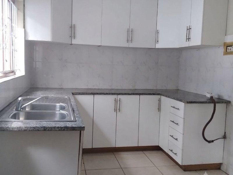 A clean, functional kitchen featuring white cabinetry, granite countertops, a double stainless steel sink, and tiled flooring, ready for personalization.