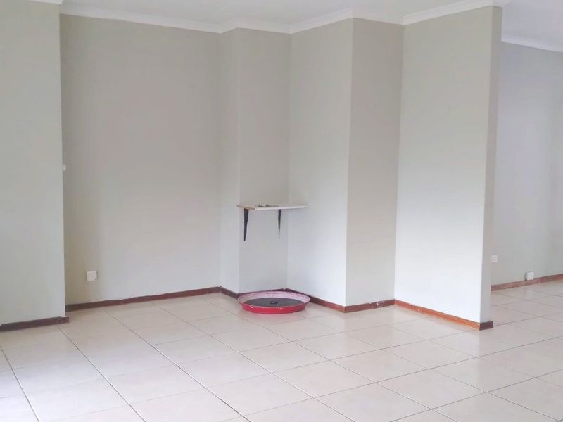 An empty, open-plan living area featuring neutral wall tones, tiled flooring, and a ceiling fan, offering a blank canvas for interior design.