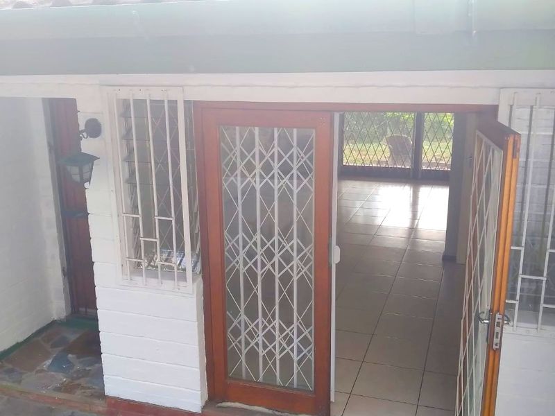 Rear exterior view showing a tiled patio entrance with security gates, leading into an interior space with ceramic floor tiles.